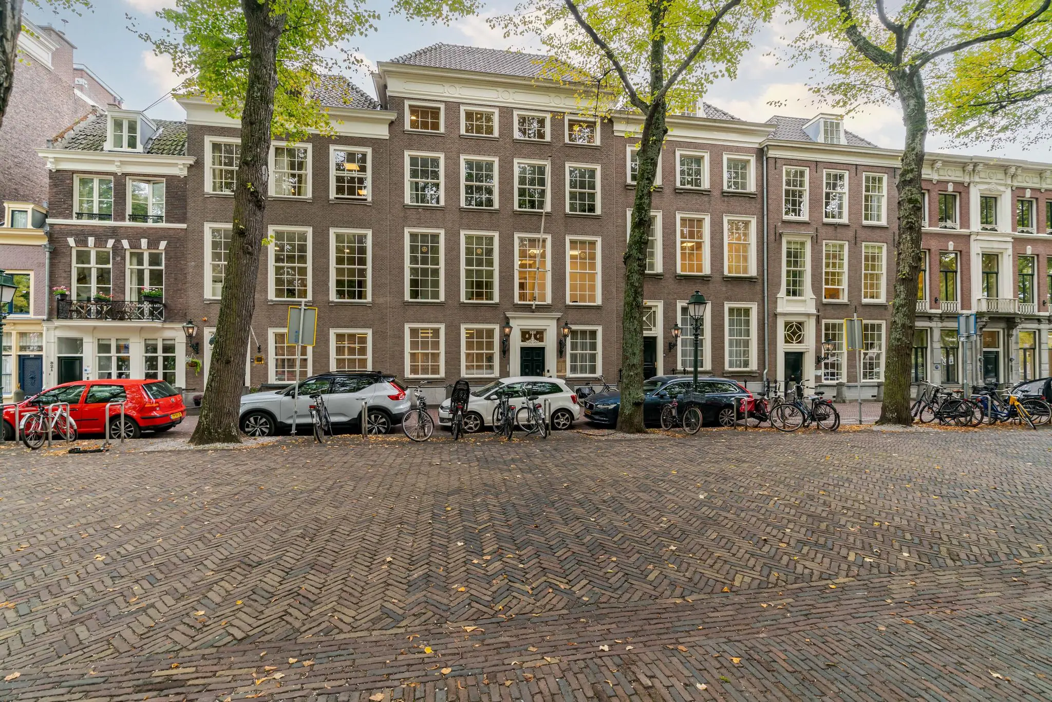 Gevels van historische panden aan het Lange Voorhout in Den Haag met geparkeerde auto's en fietsen op de voorgrond.